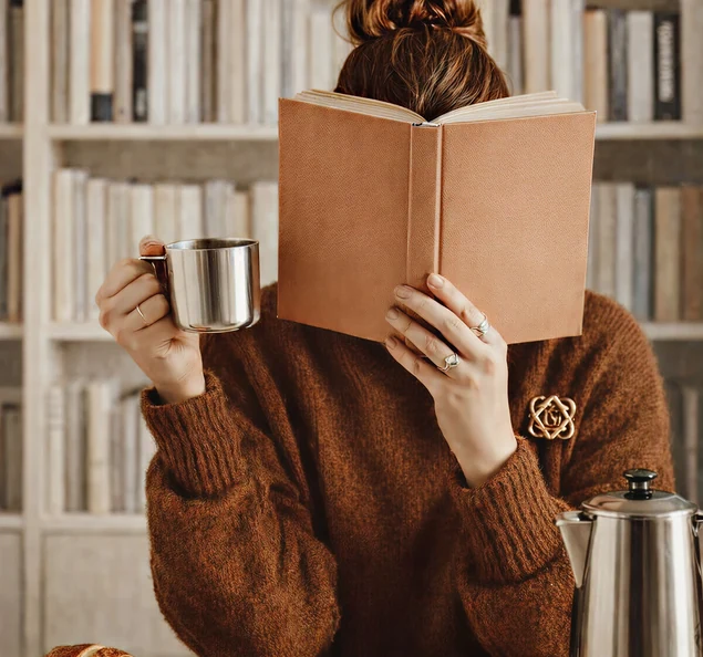 A reader holding an open book and a mug